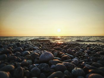 Pebbles on beach against sky during sunset