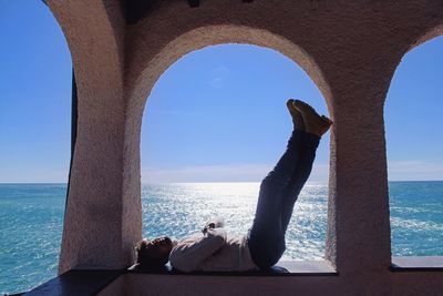 Side view of man lying on retaining wall against sea