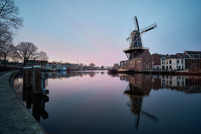 Reflection of traditional windmill and buildings in river at sunset