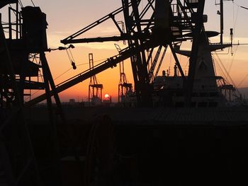 Silhouette cranes against sky at sunset