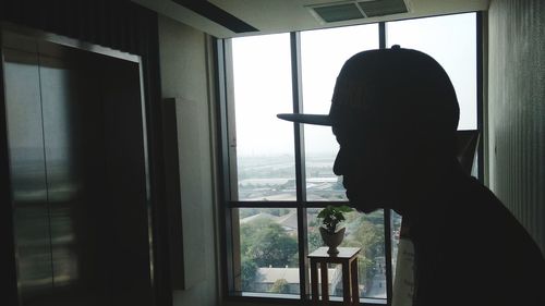 Portrait of silhouette man looking through window at home