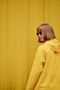 Young woman wearing sunglasses standing against yellow curtain