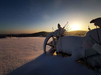 Bicycles on snow covered land against sky during sunset