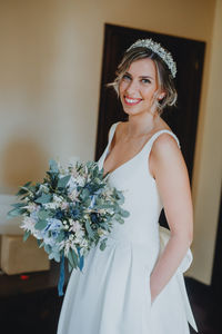 Portrait of bride holding bouquet standing against wall