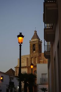 Low angle view of illuminated street light by building against sky