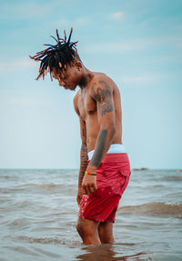 Full length of shirtless man standing at beach against sky