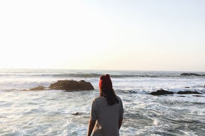 Rear view of woman standing on beach against clear sky