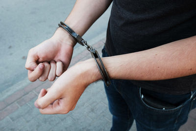 Young offender in handcuffs on wrists standing on street