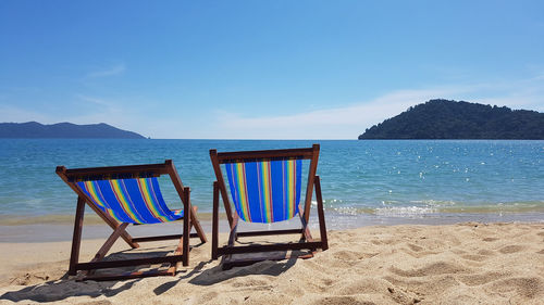 Chairs on beach against blue sky