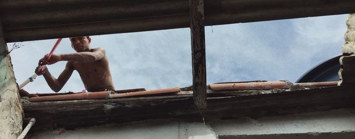 Low angle view of shirtless man on window against sky