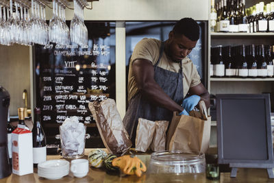 Male owner packing order in paper bag at deli store