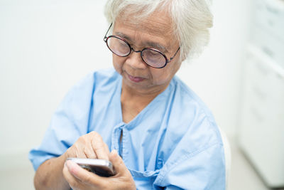 Asian senior woman wearing eyeglasses use mobile phone in hospital.