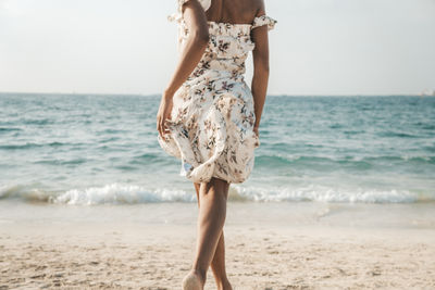 Midsection of woman at beach against sky