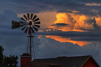Traditional windmill by buildings against sky during sunset