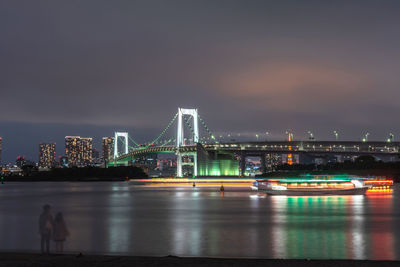 Illuminated bridge over river with city in background