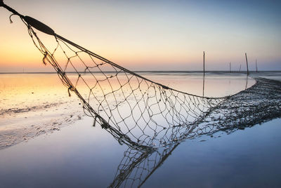 Fishing net at seashore against sky during sunset