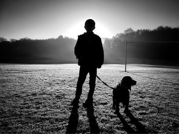 Rear view of boy with dog standing on field