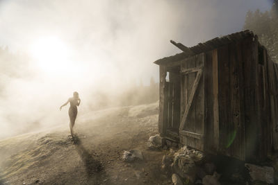 Silhouette woman walking towards old wooden hut on mountain during foggy weather