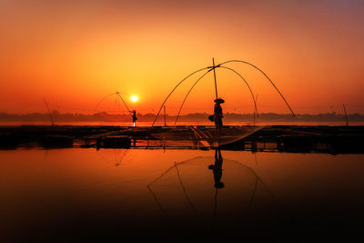 Silhouette fishing net on sea against sky during sunset