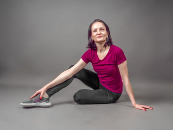 Portrait of young woman exercising against gray background