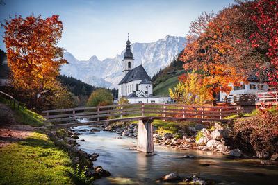 Water flowing amidst trees and buildings against sky during autumn