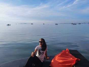 Young woman sitting on sea against sky