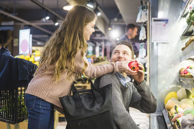 Side view of smiling daughter giving pomegranate to father while shopping in store