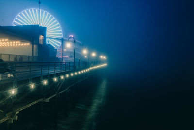 Illuminated ferris wheel against blue sky at night