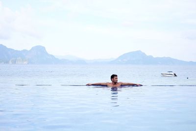 Man swimming in infinity pool by sea against sky