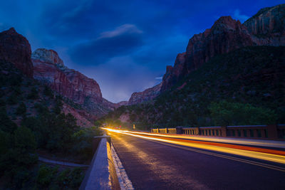 Light trails on road amidst rock formation against sky