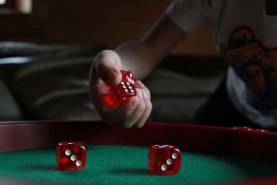 Cropped hand of child holding red dice over table