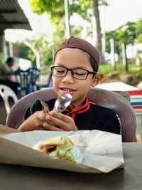 Cute smiling boy holding cutlery while eating food in outdoor restaurant