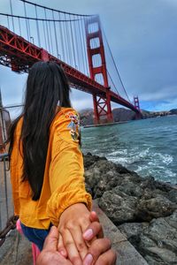 Rear view of woman holding hands while standing by sea