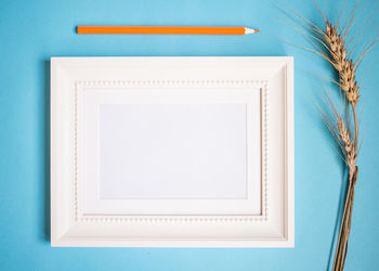 Directly above shot of blank picture frame and colored pencil on blue background