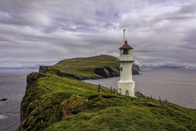 Lighthouse on mountain by sea against cloudy sky