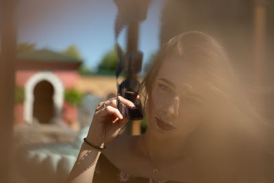 Portrait of woman holding film reel against sky