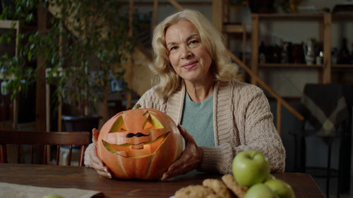 Portrait of smiling young woman holding pumpkin in kitchen