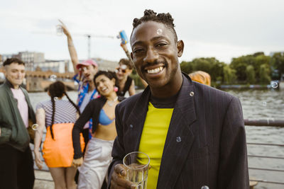 Portrait of smiling non-binary person holding drink glass with friends enjoying in background