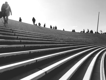 Low angle view of people walking on steps against clear sky during sunny day