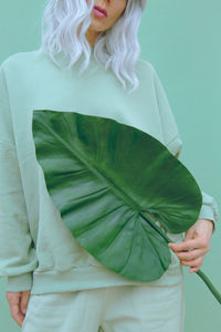 Midsection of woman holding leaf while standing over green background