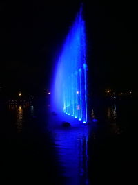 Illuminated fountain by river against sky at night
