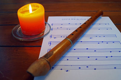 Close-up of flute on sheet music by illuminated candle on wooden table