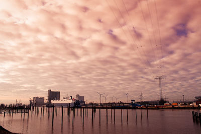 Low angle view of clouds over sea and cityscape during sunset