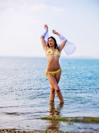 Seductive young woman in bikini standing at beach against sky