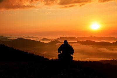 Silhouette man standing on mountain against orange sky