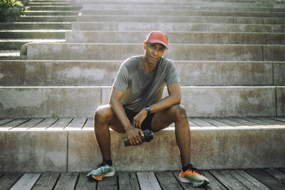 Portrait of exhausted man holding shaker bottle while sitting on steps