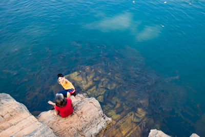 High angle view of people sitting on rock by lake