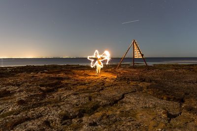 Person light painting at beach against sky at night
