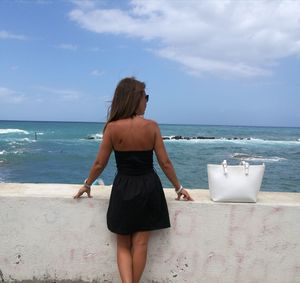 Rear view of woman standing at beach against sky