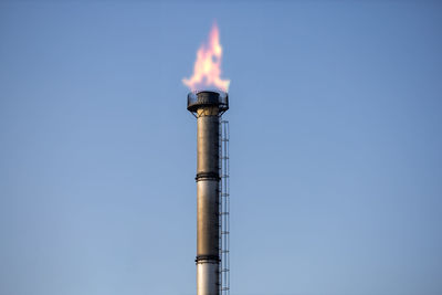 Low angle view of smoke stack against clear blue sky